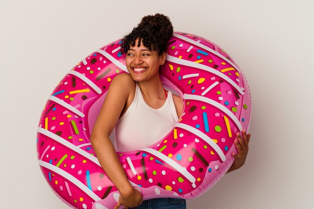 Joven mujer de raza mixta sosteniendo una rosquilla de aire inflable aislado sobre fondo blanco soñando con lograr metas y propósitos