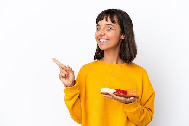 Foto joven mujer de raza mixta sosteniendo sashimi aislado sobre fondo blanco apuntando hacia el lado para presentar un producto
