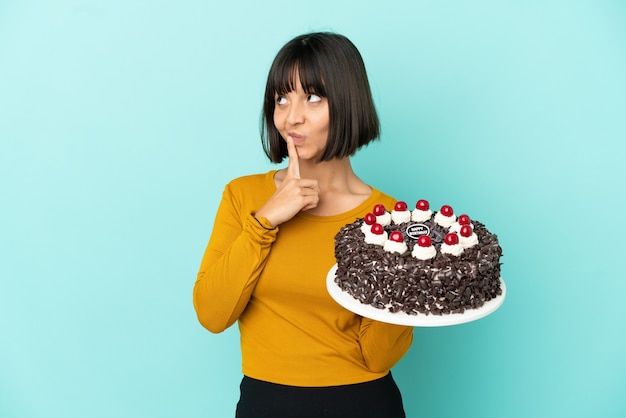 Joven mujer de raza mixta sosteniendo la torta de cumpleaños con dudas mientras mira hacia arriba