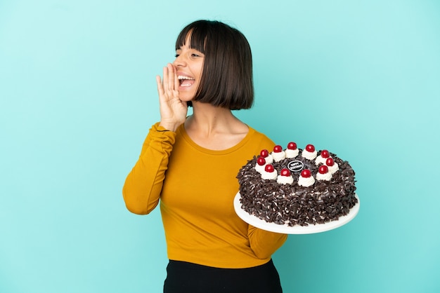 Joven mujer de raza mixta sosteniendo la torta de cumpleaños gritando con la boca abierta hacia el lado