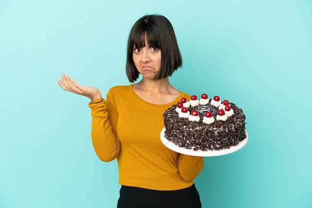 Joven mujer de raza mixta sosteniendo la torta de cumpleaños haciendo gesto de dudas