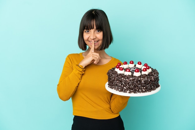 Joven mujer de raza mixta sosteniendo la torta de cumpleaños mostrando un gesto de silencio poniendo el dedo en la boca