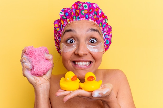 Joven mujer de raza mixta tomando un baño sosteniendo una esponja y patos de goma