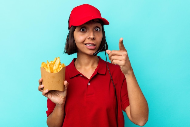 Joven mujer de raza mixta trabajador de restaurante de comida rápida sosteniendo papas fritas aislado sobre fondo azul con una idea, concepto de inspiración.