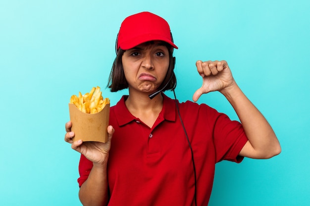 Joven mujer de raza mixta trabajador de restaurante de comida rápida sosteniendo papas fritas aislado sobre fondo azul mostrando un gesto de aversión, pulgares hacia abajo. Concepto de desacuerdo.