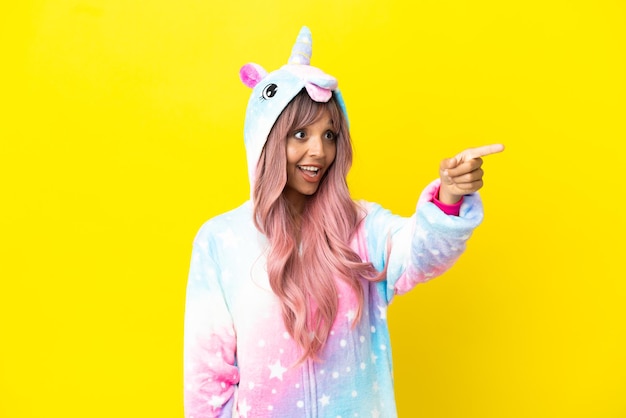 Joven mujer de raza mixta vistiendo un pijama de unicornio aislado sobre fondo blanco apuntando hacia afuera