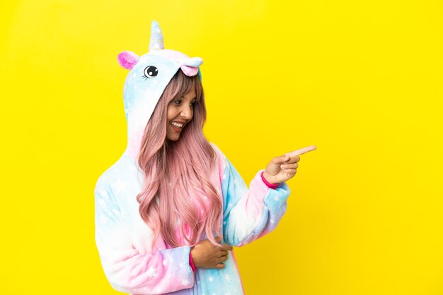 Joven mujer de raza mixta vistiendo un pijama de unicornio aislado sobre fondo blanco apuntando con el dedo hacia un lado y presentando un producto