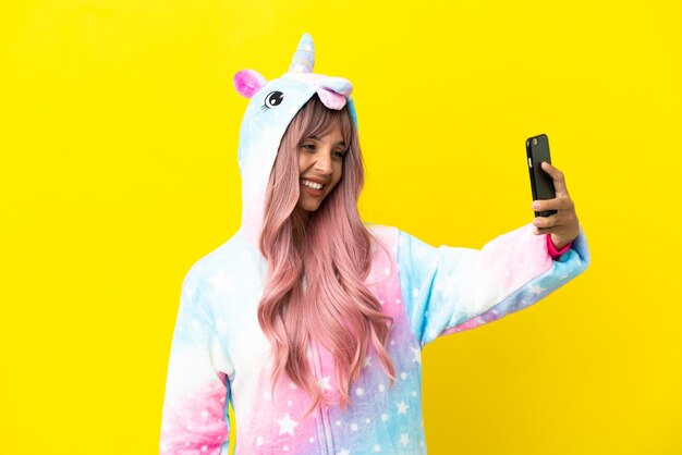 Joven mujer de raza mixta vistiendo un pijama de unicornio aislado sobre fondo blanco haciendo un selfie