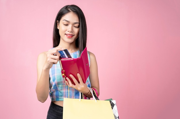 Joven mujer recogiendo una tarjeta de crédito de su bolso con una sonrisa y llevando bolsas de compras,