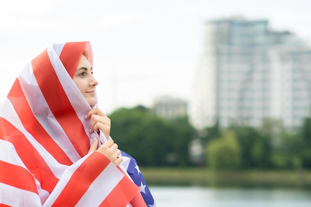 Joven mujer refugiada feliz con la bandera nacional de Estados Unidos en la cabeza y los hombros Chica musulmana positiva que viaja en Estados Unidos