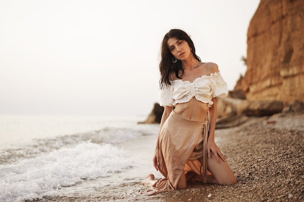 Joven mujer relajada sentada sola en la playa vacía