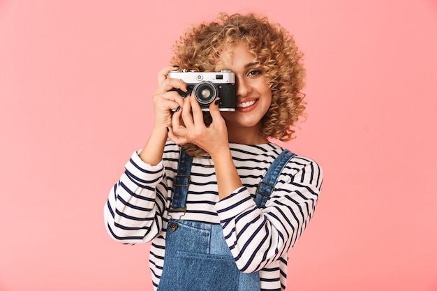 Joven mujer rizada 20s photopraphing en cámara retro mientras está de pie