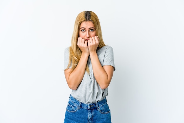 Joven mujer rubia aislada en blanco mordiendo las uñas