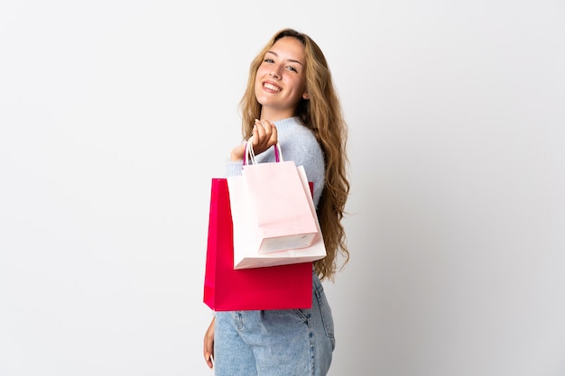 Joven mujer rubia aislada en blanco sosteniendo bolsas de la compra y sonriendo