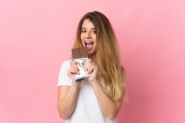 Foto joven mujer rubia aislada comiendo una tableta de chocolate