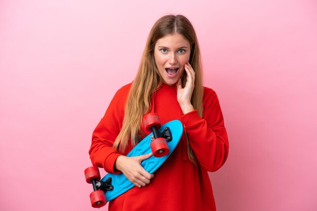 Joven mujer rubia aislada de fondo rosa con un patín y haciendo un gesto sorpresa