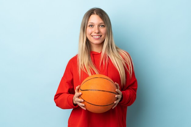 Joven mujer rubia aislada en la pared azul jugando baloncesto