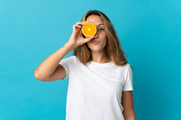 Joven mujer rubia aislada en la pared azul sosteniendo una naranja