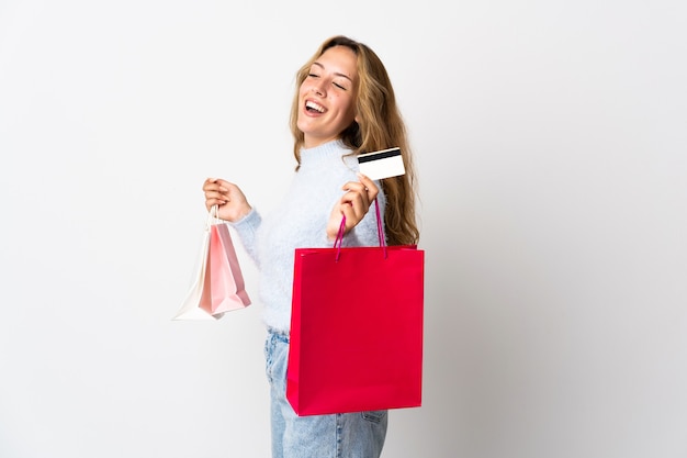 Joven mujer rubia aislada en la pared blanca con bolsas de la compra y una tarjeta de crédito