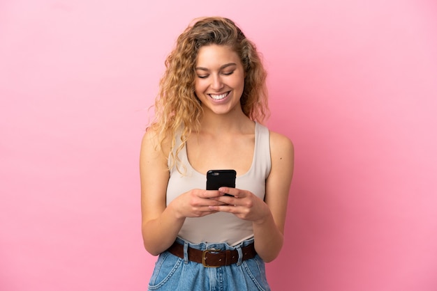 Joven mujer rubia aislada sobre fondo rosa enviando un mensaje o correo electrónico con el móvil