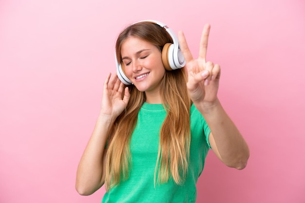 Joven mujer rubia aislada sobre fondo rosa escuchando música y cantando