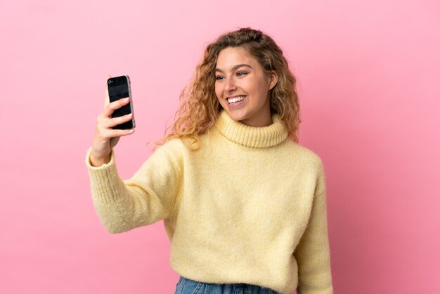 Joven mujer rubia aislada sobre fondo rosa haciendo un selfie