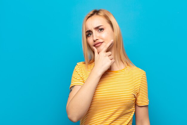 Joven mujer rubia de aspecto serio, pensativo y desconfiado, con un brazo cruzado y la mano en el mentón, ponderación de opciones