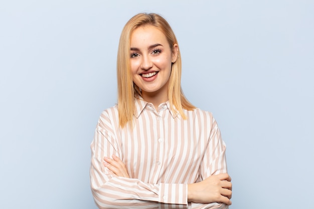 Joven mujer rubia con aspecto de un triunfador feliz, orgulloso y satisfecho sonriendo con los brazos cruzados