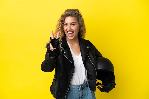 Joven mujer rubia con un casco de moto aislado sobre fondo amarillo