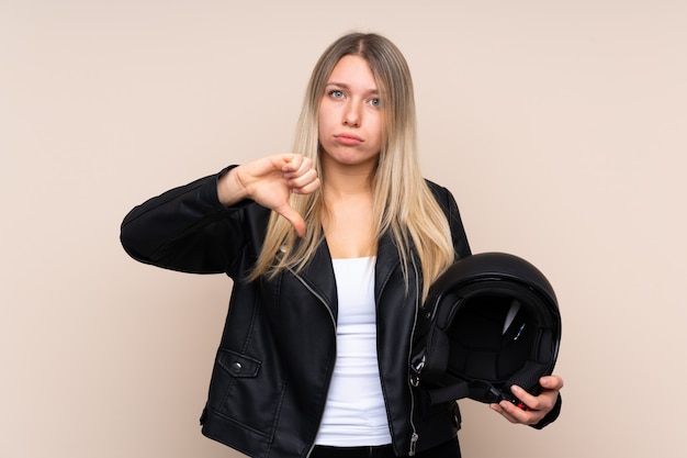 Joven mujer rubia con un casco de moto mostrando el pulgar hacia abajo signo