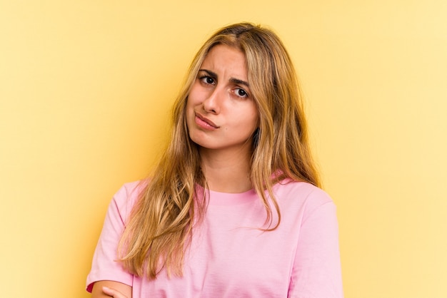 Joven mujer rubia caucásica aislada sobre fondo amarillo infeliz mirando a puerta cerrada con expresión sarcástica.