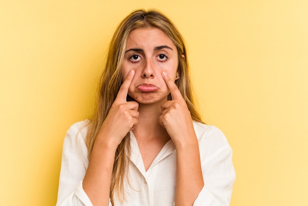 Joven mujer rubia caucásica aislada sobre fondo amarillo llorando, infeliz con algo, concepto de agonía y confusión.