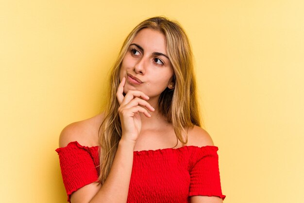 Joven mujer rubia caucásica aislada sobre fondo amarillo mirando hacia los lados con expresión dudosa y escéptica.