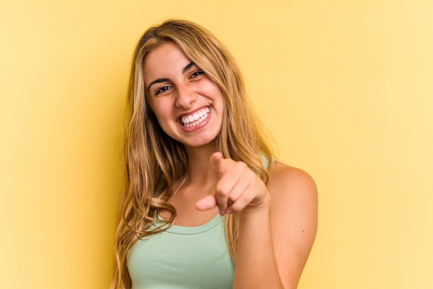 Joven mujer rubia caucásica aislada sobre fondo amarillo sonrisas alegres apuntando al frente.