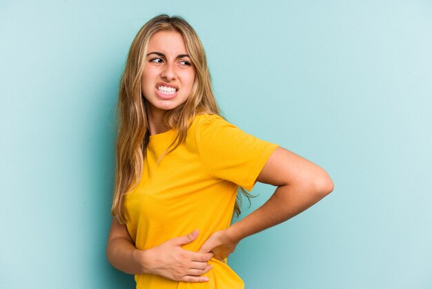 Joven mujer rubia caucásica aislada sobre fondo azul que sufre un dolor de espalda.