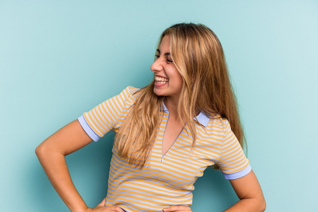 Joven mujer rubia caucásica aislada sobre fondo azul se ríe felizmente y se divierte manteniendo las manos sobre el estómago.