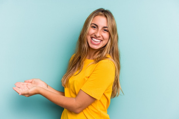 Joven mujer rubia caucásica aislada sobre fondo azul sosteniendo un espacio de copia en una palma.