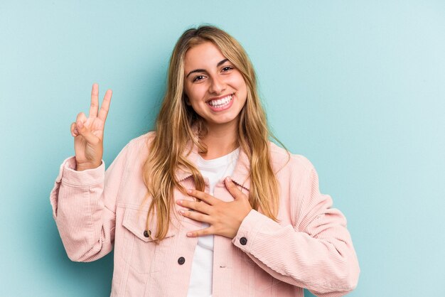 Joven mujer rubia caucásica aislada sobre fondo azul tomando un juramento, poniendo la mano en el pecho.