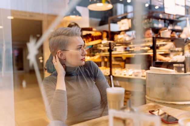 Joven mujer rubia caucásica grabando mensajes de audio con smartphone sentado en el café