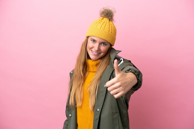 Joven mujer rubia con chaqueta de invierno aislada de fondo rosa con los pulgares hacia arriba porque algo bueno ha sucedido