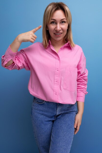 Joven mujer rubia elegante y agradable está vestida con una camisa rosa y jeans gesticulando con las manos