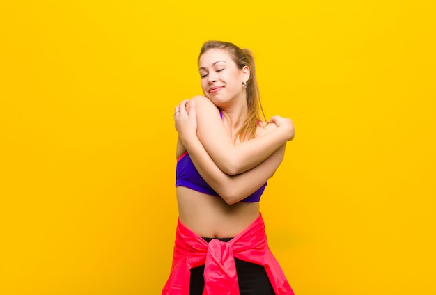 Joven mujer rubia enamorada, sonriendo, abrazándose y abrazándose a sí misma, permaneciendo soltera, siendo egoísta y egocéntrica. concepto de deporte