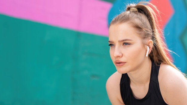 Joven mujer rubia enfocada en el entrenamiento al aire libre descansando después de correr, fondo multicolor