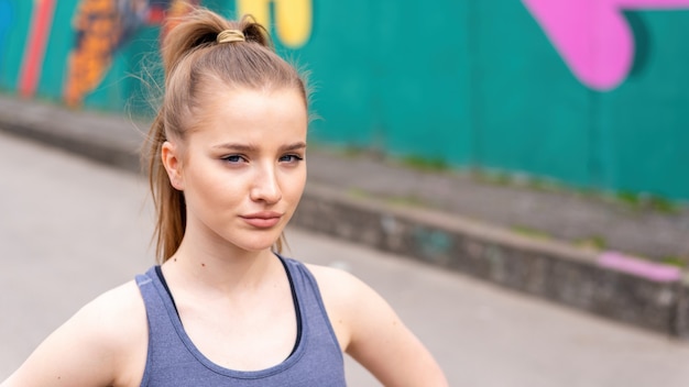 Joven mujer rubia enfocada en ropa deportiva en el entrenamiento al aire libre, fondo multicolor