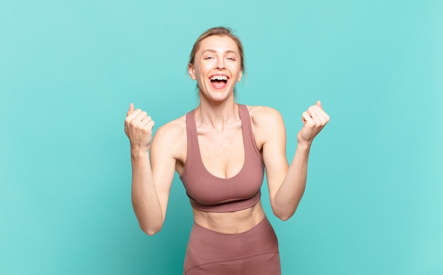 Joven mujer rubia gritando triunfalmente, riendo y sintiéndose feliz y emocionada mientras celebra el éxito. concepto de deporte