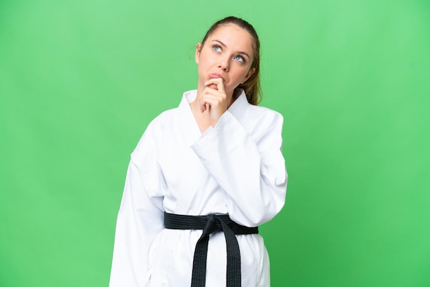 Joven mujer rubia haciendo karate sobre un fondo clave de croma aislado que tiene dudas