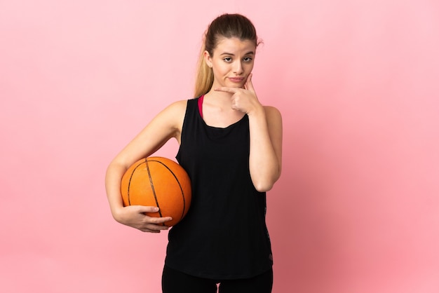 Joven mujer rubia jugando baloncesto aislado en el pensamiento de pared rosa