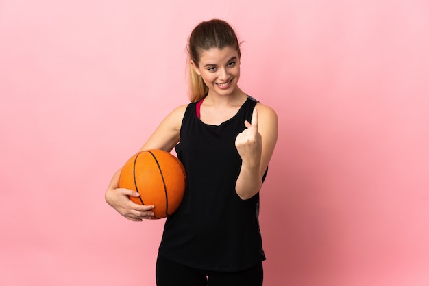 Joven mujer rubia jugando baloncesto aislado en rosa haciendo gesto que viene