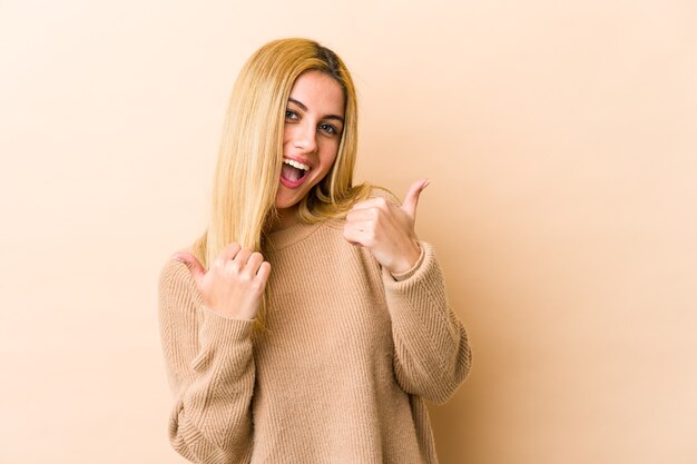 Joven mujer rubia levantando ambos pulgares, sonriente y confiada