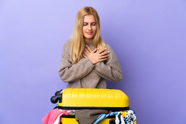 Joven mujer rubia con una maleta llena de ropa aislada